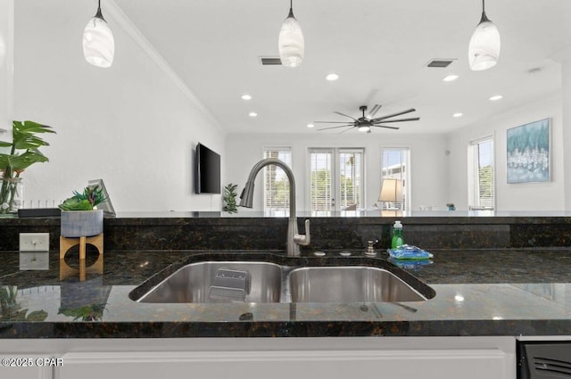 kitchen with decorative light fixtures, a wealth of natural light, dark stone counters, and sink