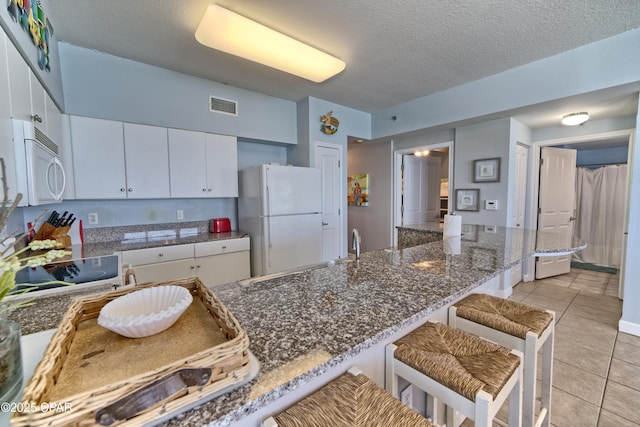 kitchen featuring light tile patterned floors, white appliances, a kitchen breakfast bar, white cabinets, and visible vents