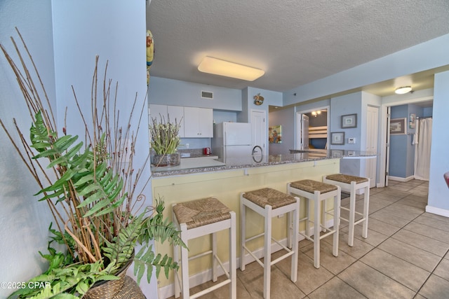 kitchen with white cabinetry, white fridge, a textured ceiling, a breakfast bar, and light tile patterned floors