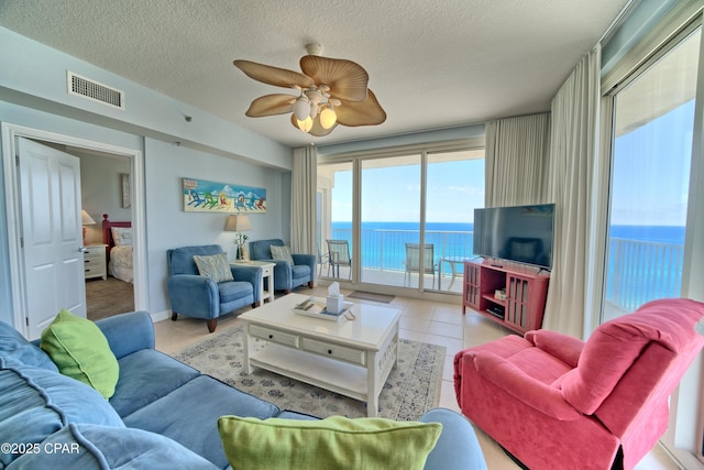 living room featuring tile patterned floors, visible vents, a textured ceiling, and ceiling fan