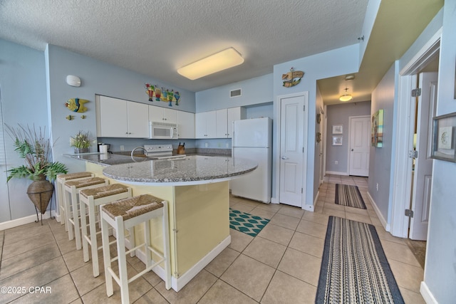 kitchen with kitchen peninsula, a kitchen breakfast bar, light stone counters, white appliances, and white cabinets