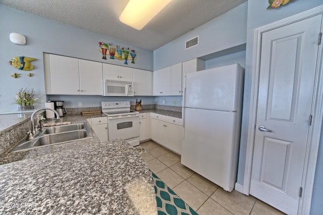 kitchen with white appliances, dark countertops, white cabinets, visible vents, and a sink