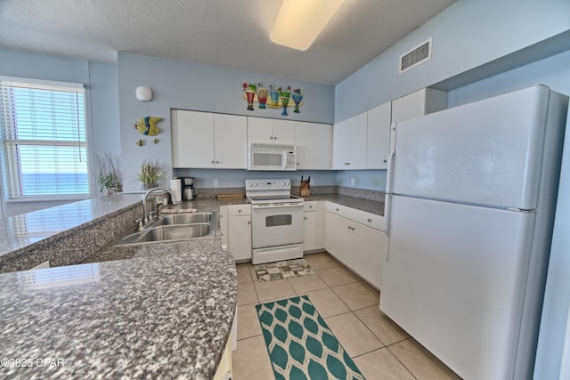 kitchen with visible vents, a sink, dark countertops, white appliances, and white cabinetry