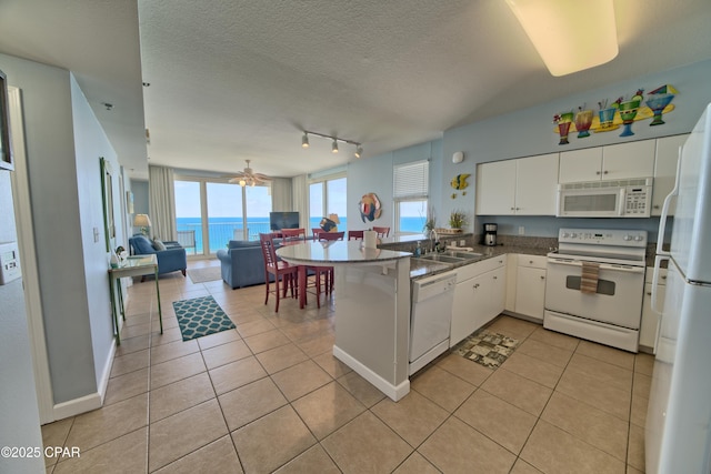 kitchen featuring open floor plan, a peninsula, light tile patterned flooring, and white appliances