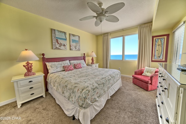 carpeted bedroom with multiple windows, ceiling fan, a water view, and a textured ceiling