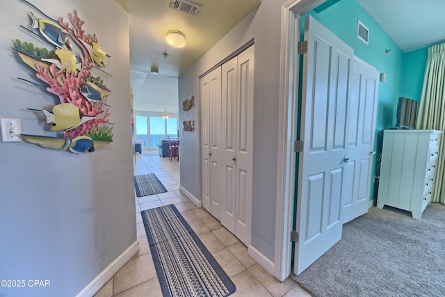 hallway with light tile patterned floors, visible vents, and baseboards