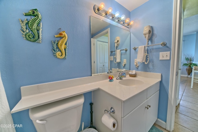 half bath featuring toilet, tile patterned floors, vanity, and baseboards