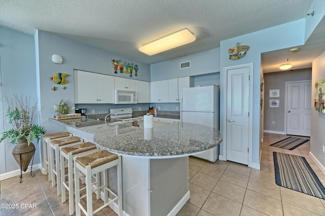 kitchen with white appliances, a peninsula, visible vents, a breakfast bar, and light tile patterned flooring