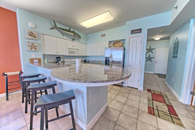 kitchen featuring light tile patterned flooring, kitchen peninsula, white appliances, a breakfast bar, and white cabinets