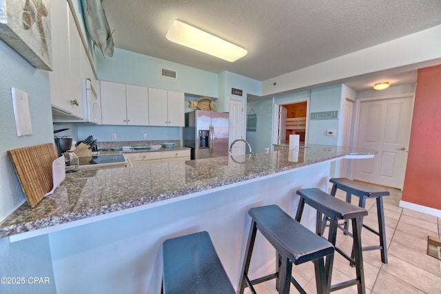 kitchen with a breakfast bar, kitchen peninsula, stainless steel fridge with ice dispenser, light tile patterned floors, and white cabinetry