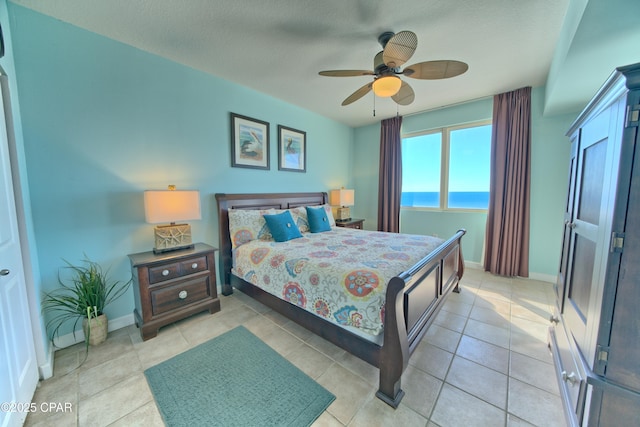 bedroom featuring ceiling fan, a water view, light tile patterned floors, and a textured ceiling