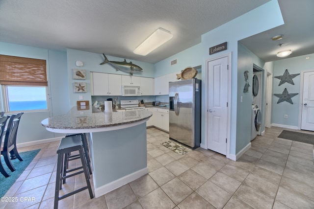 kitchen featuring white appliances, a peninsula, stone counters, white cabinets, and a breakfast bar area