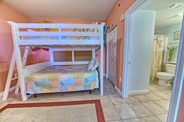bedroom featuring ensuite bathroom, a textured ceiling, a closet, tile patterned flooring, and visible vents