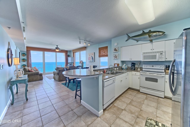 kitchen with white appliances, a peninsula, white cabinets, a sink, and open floor plan