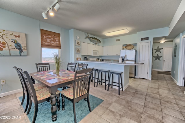 dining space with light tile patterned floors, visible vents, a textured ceiling, and track lighting
