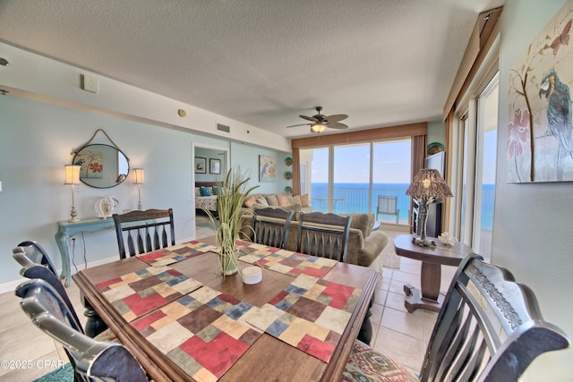 dining area featuring light tile patterned floors, a textured ceiling, a ceiling fan, visible vents, and a water view