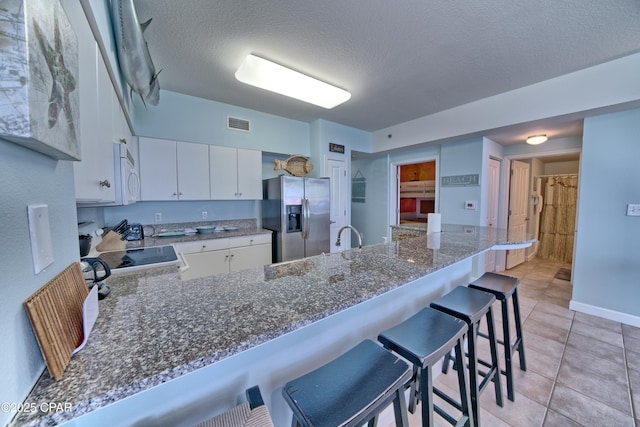 kitchen featuring a kitchen breakfast bar, white appliances, a peninsula, a textured ceiling, and visible vents