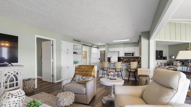 living room featuring dark wood-type flooring, a barn door, and a textured ceiling