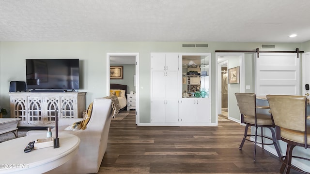 living room featuring a barn door, dark hardwood / wood-style flooring, and a textured ceiling