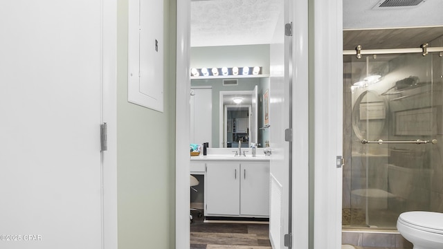 bathroom featuring hardwood / wood-style flooring, vanity, toilet, a shower with door, and a textured ceiling