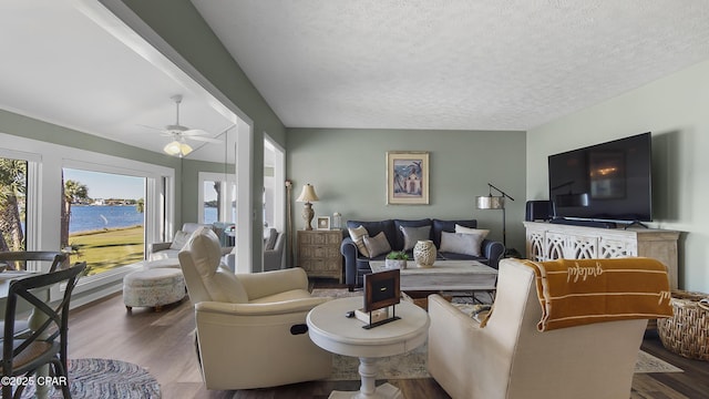 living room featuring dark hardwood / wood-style flooring, a water view, ceiling fan, and a textured ceiling