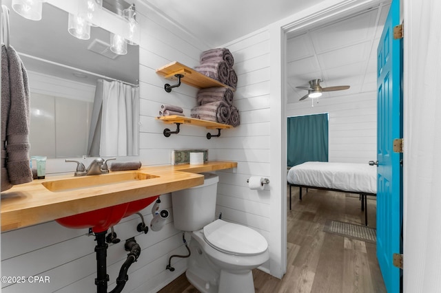 bathroom with ceiling fan, sink, toilet, wood walls, and hardwood / wood-style flooring