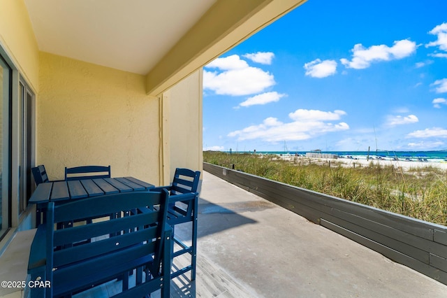 view of patio / terrace featuring a water view, a balcony, and a beach view