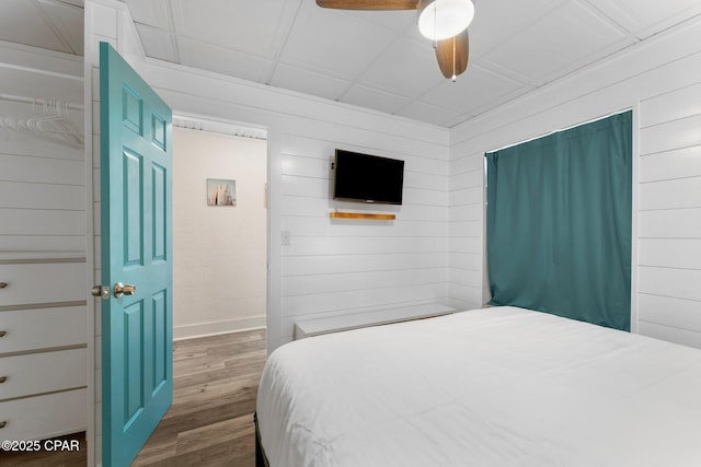 bedroom featuring ceiling fan, dark hardwood / wood-style flooring, and wood walls