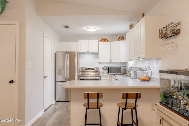 kitchen featuring tasteful backsplash, a kitchen breakfast bar, kitchen peninsula, white cabinets, and appliances with stainless steel finishes