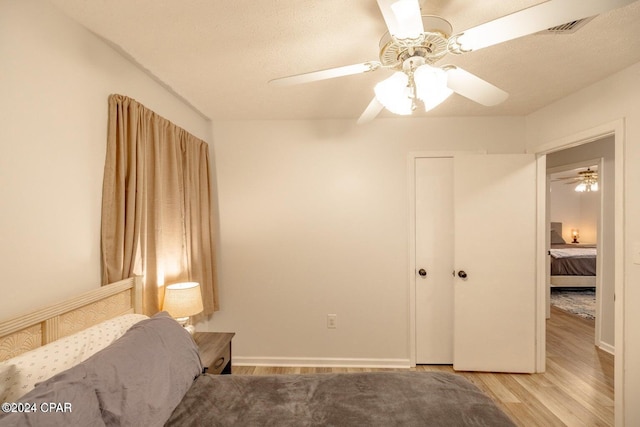 bedroom with a textured ceiling, ceiling fan, light hardwood / wood-style flooring, and a closet