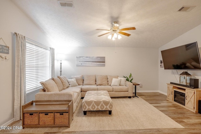 living room featuring vaulted ceiling, ceiling fan, light hardwood / wood-style flooring, and a textured ceiling