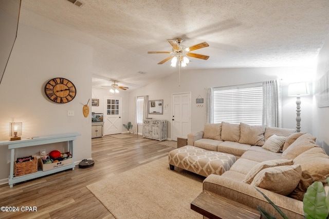 living room with light wood-type flooring, a textured ceiling, vaulted ceiling, and ceiling fan