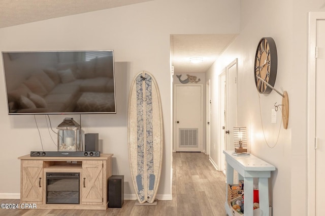 hallway featuring a textured ceiling, light hardwood / wood-style flooring, and lofted ceiling