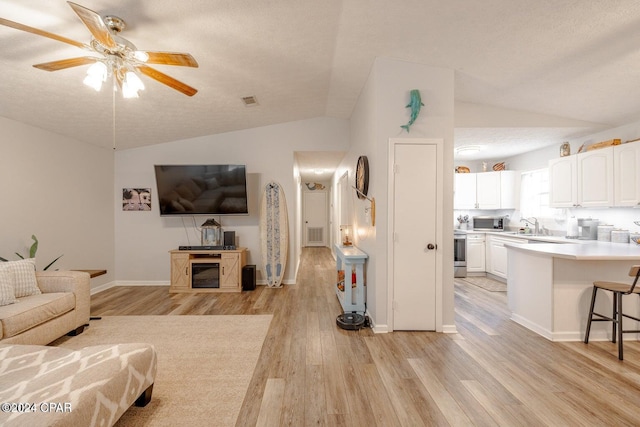 living room with a textured ceiling, vaulted ceiling, ceiling fan, sink, and light hardwood / wood-style floors