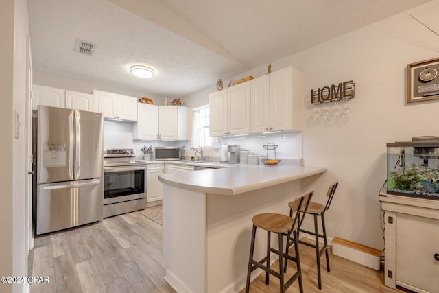 kitchen with white cabinetry, a breakfast bar, light hardwood / wood-style flooring, and appliances with stainless steel finishes