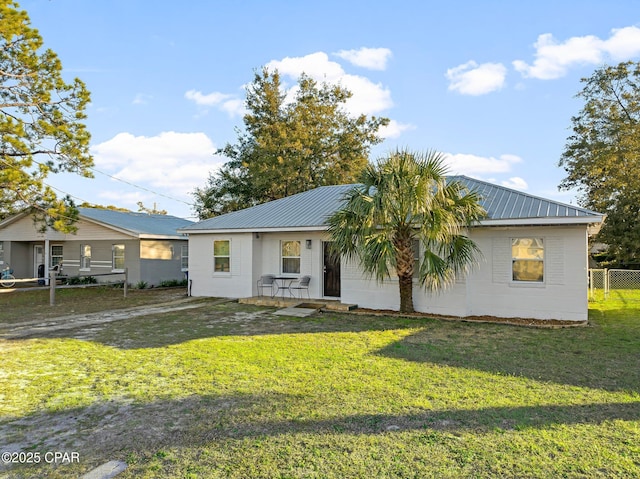 single story home featuring metal roof, a front lawn, concrete block siding, and fence