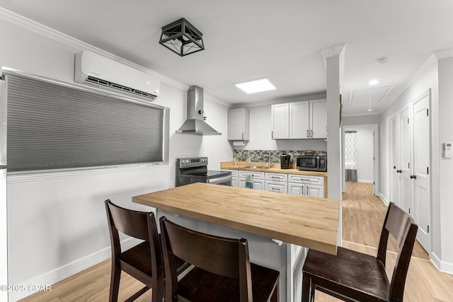 kitchen with butcher block countertops, stainless steel range with electric cooktop, an AC wall unit, wall chimney range hood, and a kitchen bar