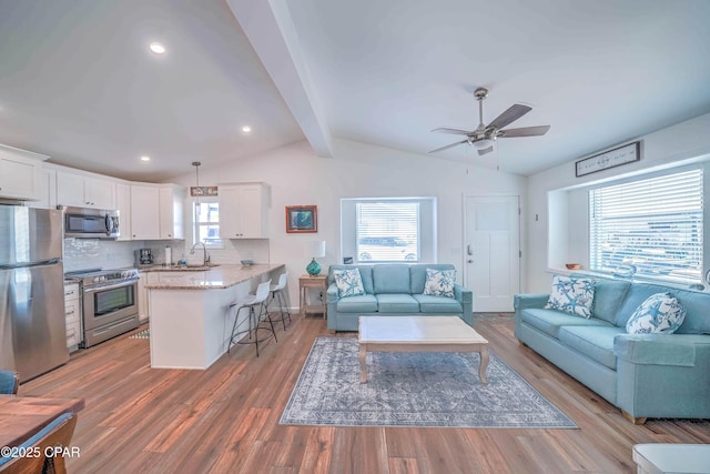 living room with hardwood / wood-style floors, sink, ceiling fan, vaulted ceiling with beams, and a wealth of natural light