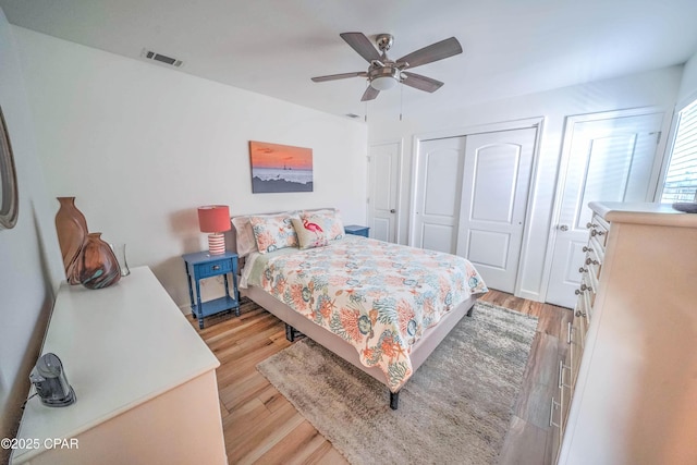 bedroom with light wood-type flooring, two closets, and ceiling fan