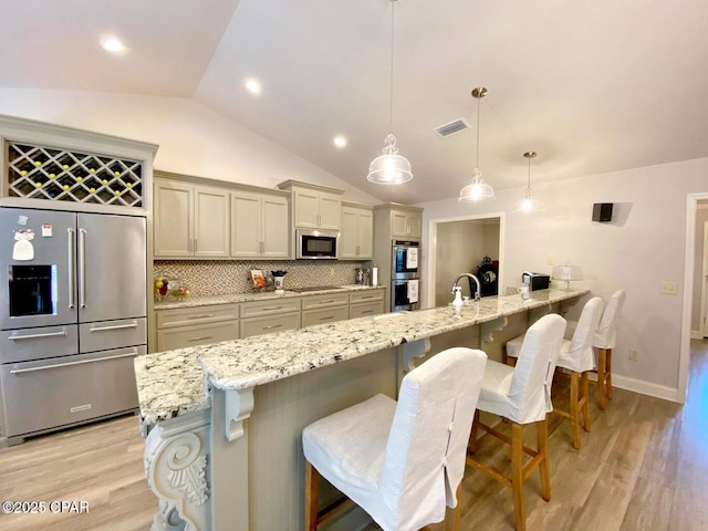 kitchen featuring appliances with stainless steel finishes, lofted ceiling, tasteful backsplash, hanging light fixtures, and a breakfast bar