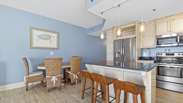 kitchen with appliances with stainless steel finishes, light hardwood / wood-style flooring, hanging light fixtures, a kitchen breakfast bar, and dark stone countertops