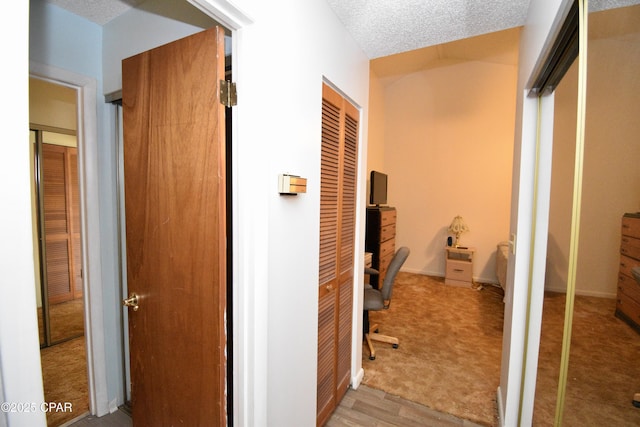 corridor with light wood-type flooring and a textured ceiling