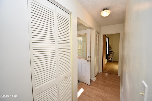 corridor with a textured ceiling and light hardwood / wood-style flooring