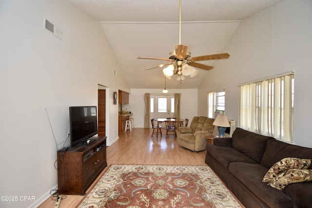 living room featuring high vaulted ceiling, light wood-type flooring, ceiling fan, and a textured ceiling