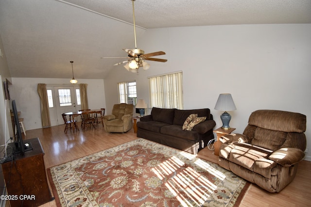 living room with ceiling fan, light wood-type flooring, lofted ceiling, and a textured ceiling