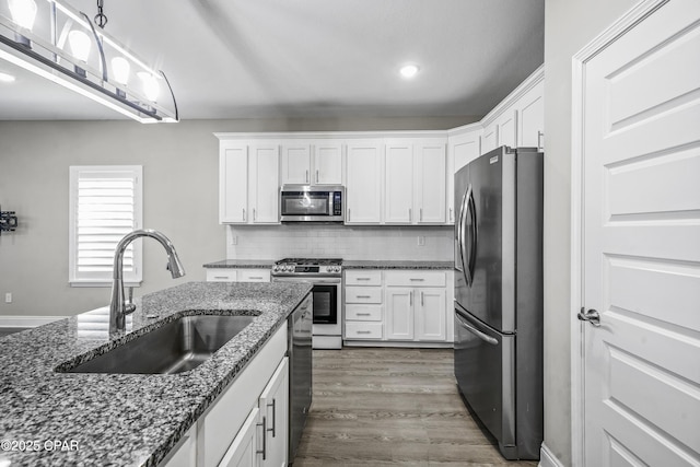 kitchen with sink, stainless steel appliances, tasteful backsplash, dark stone counters, and white cabinets