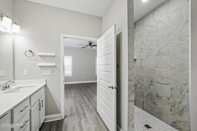 bathroom with ceiling fan, vanity, wood-type flooring, and tiled shower