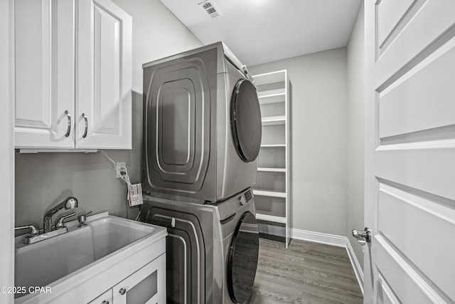 laundry room with cabinets, stacked washer and dryer, dark hardwood / wood-style floors, and sink