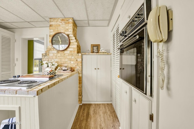 kitchen featuring white cabinets, stainless steel gas cooktop, oven, a drop ceiling, and light hardwood / wood-style flooring