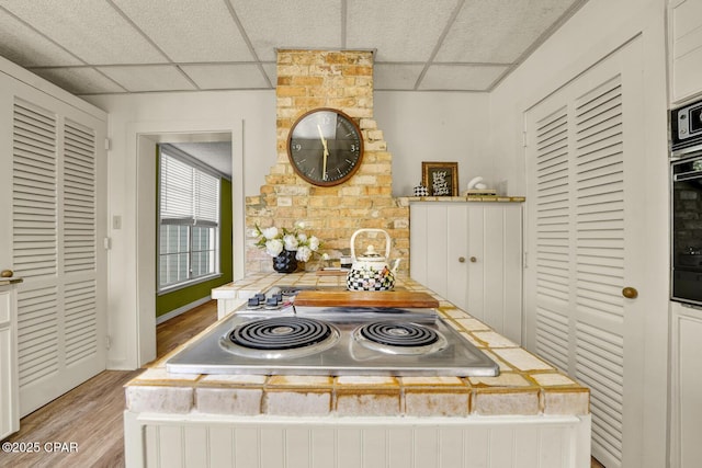 kitchen featuring light wood-type flooring, a paneled ceiling, stainless steel gas cooktop, and black oven